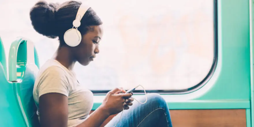 girl on train wearing headphones and looking at her phone