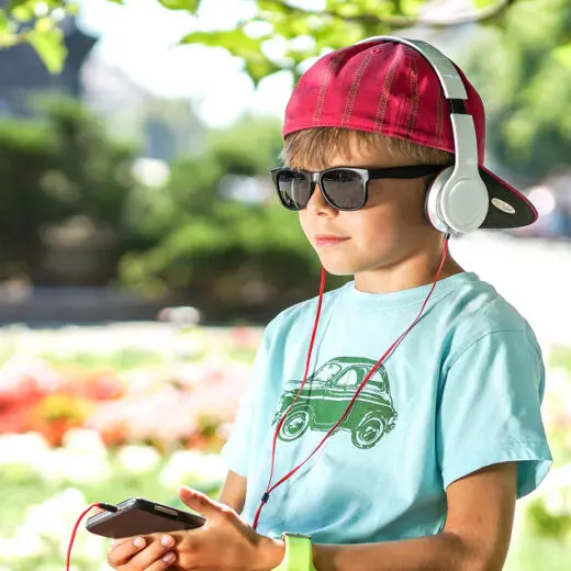 Young boy with baseball cap on backwards, sunnies and headphones, listening to a smartphone