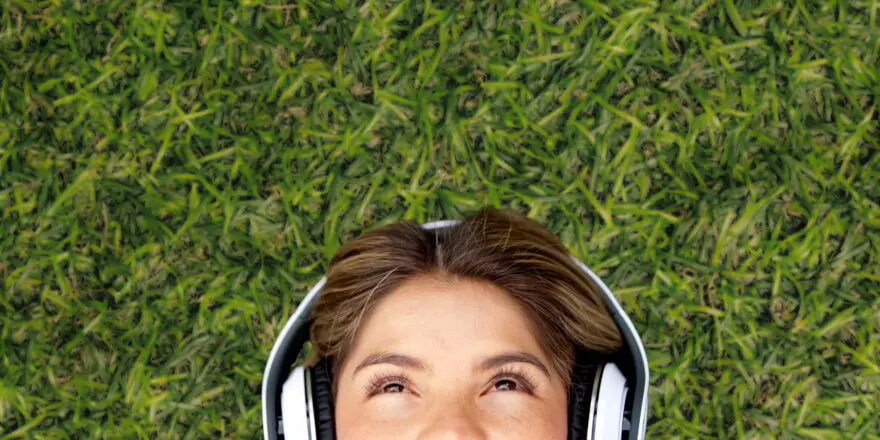 Cute young brunette woman with big white headphones lying back in the grass