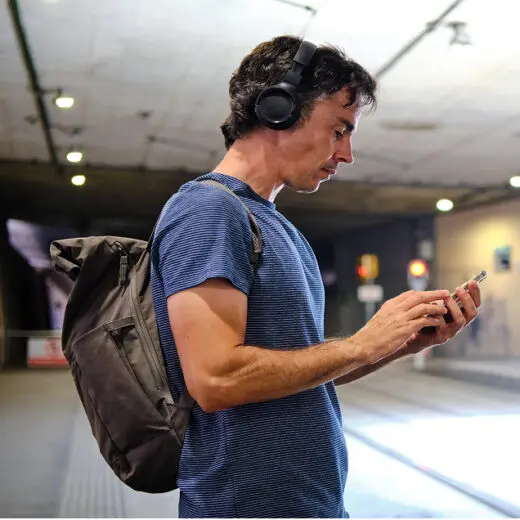 Man with rucksack on wearing headphones listening to audiobooks checking his phone at a train station