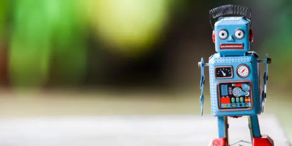 A vintage blue tin toy robot with red feet and a spring antenna, standing on a wooden surface with a soft green background.