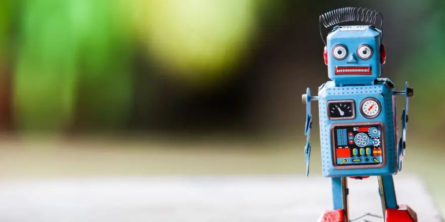 A vintage blue tin toy robot with red feet and a spring antenna, standing on a wooden surface with a soft green background.