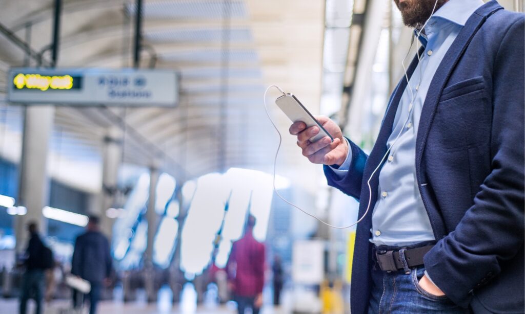 casual business man listening to headphones and looking at smartphone in train station