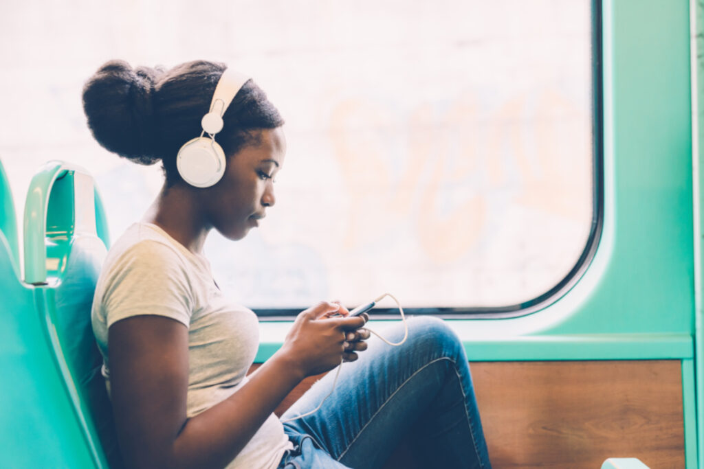 girl on train wearing headphones and looking at her phone